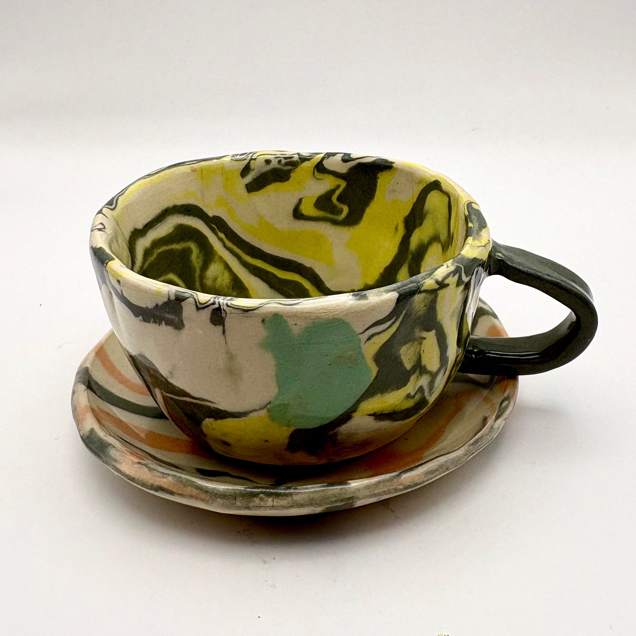 Handmade patterned ceramic plates mugs created by students in a Nerikomi workshop. Black white yellow and greem marbled latte mug and saucer set