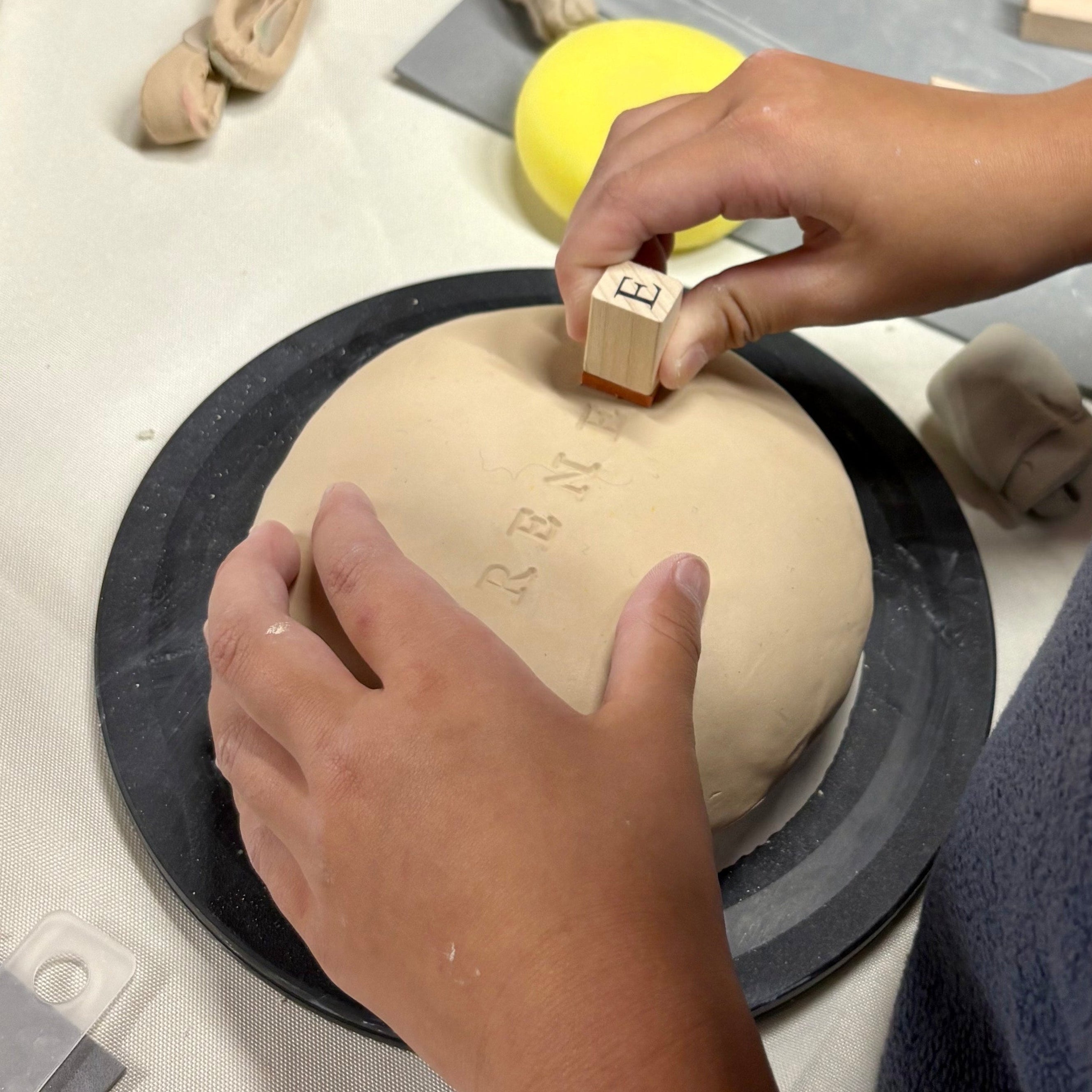 Person stamping a design onto a clay sheet with a wooden block