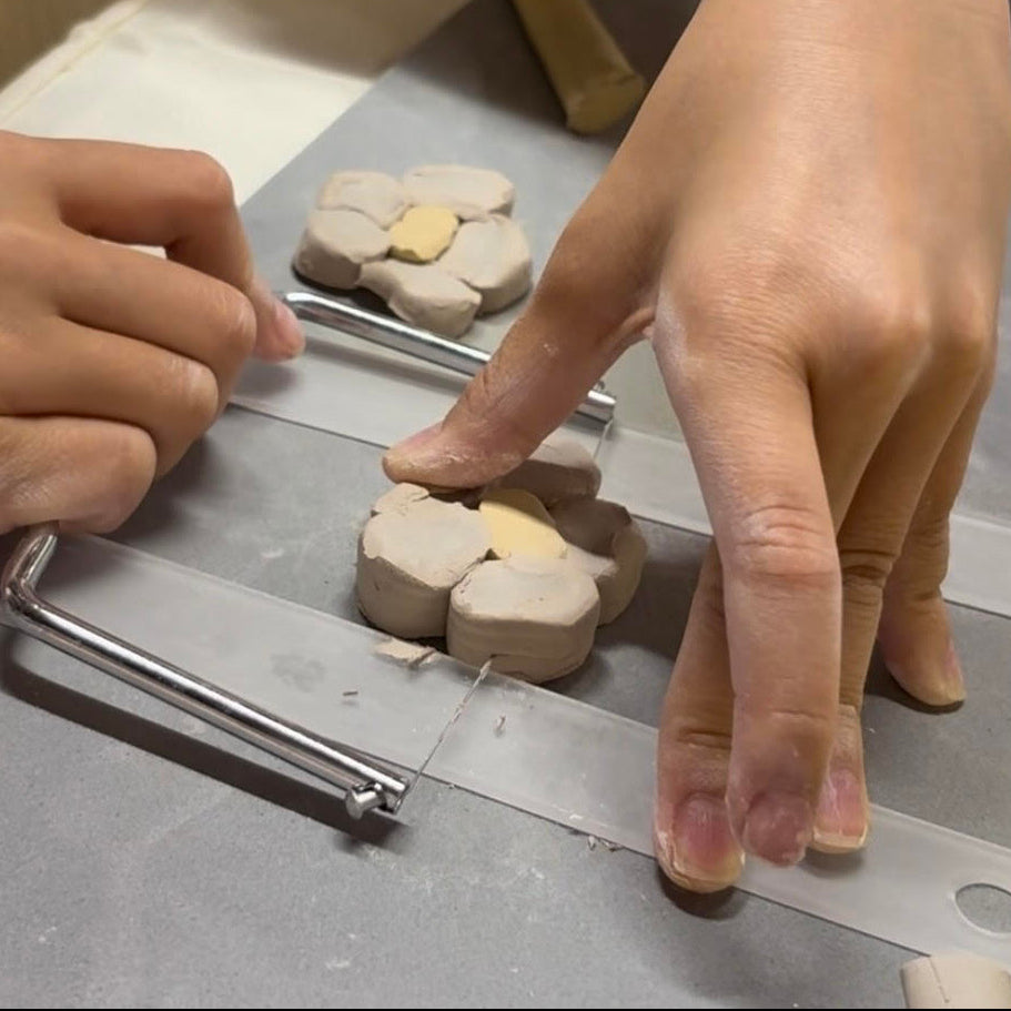 Hands using a cookie cutter to shape clay into petal shapes