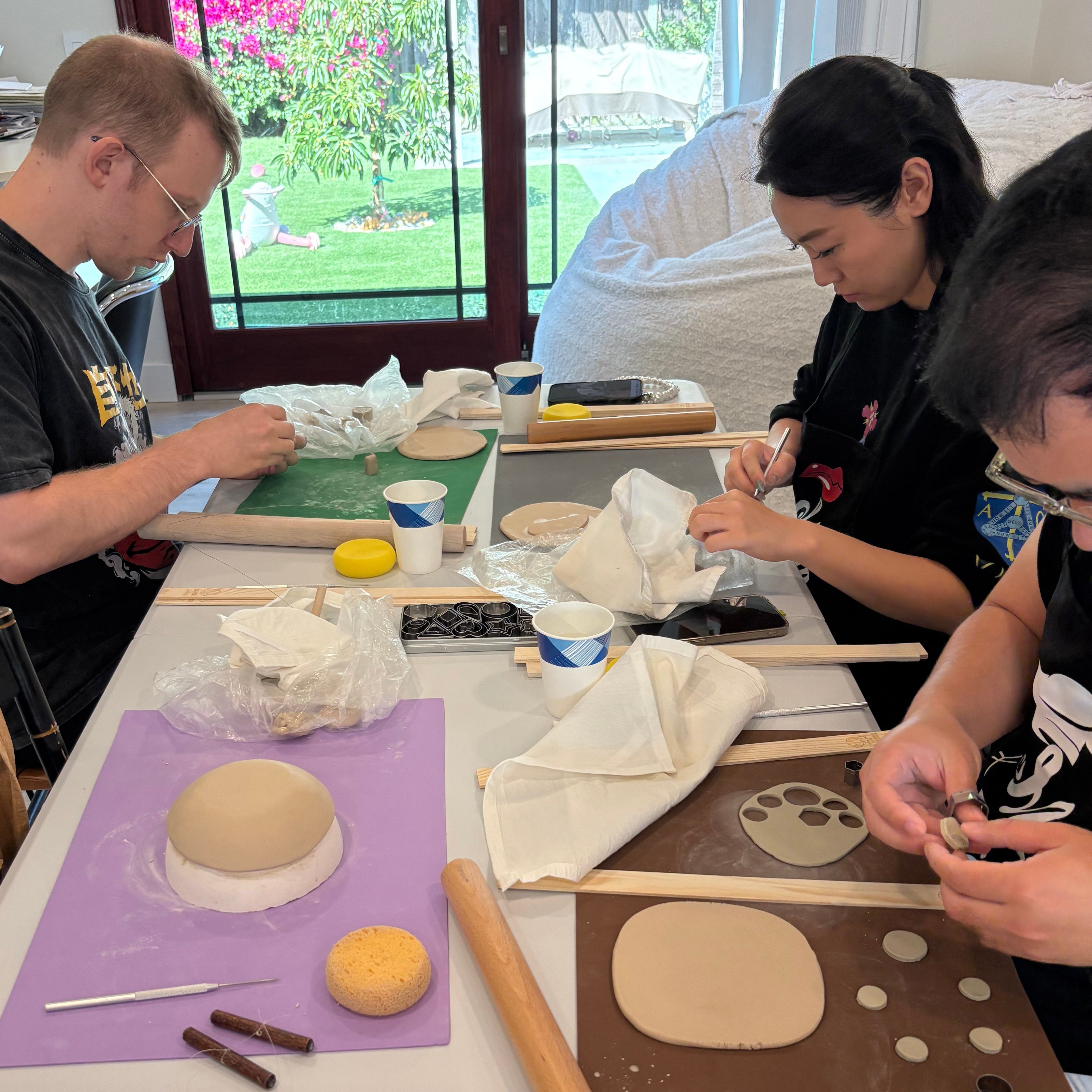 Three people working with nerikomi ceramics on a table with various tools and ingredients.